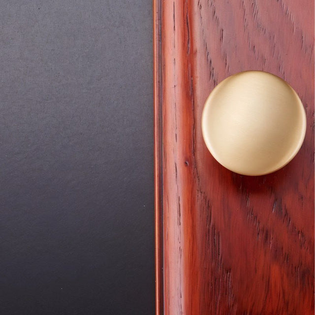 "A brass dome-shaped cabinet knob with a flared base mounted on a wooden surface, showcasing its elegant design."