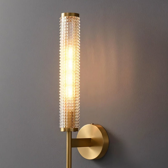 "Close-up of a modern brass wall lamp with a textured cylindrical glass shade."