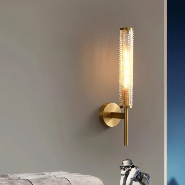 "A modern brass wall lamp with a textured glass shade casting a warm light on a gray wall."