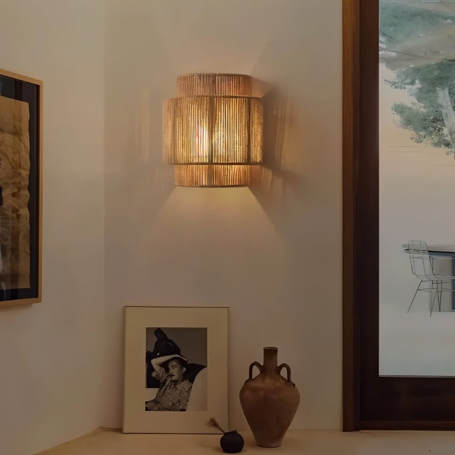 "A rustic living room featuring a layered cylindrical wall lamp made of bamboo, rattan, and hemp, casting a warm, patterned light."