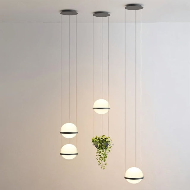 "Modern pendant lights with spherical frosted glass diffusers and iron bands, grouped with hanging planters in a high-ceiling contemporary space."