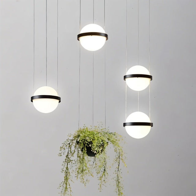 "Modern pendant lights with spherical frosted glass diffusers and iron bands, arranged in a contemporary grouping with a hanging planter."
