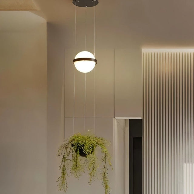 "Modern pendant light with a spherical frosted glass diffuser and iron band, combined with a hanging planter and soft ambient light."