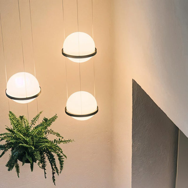 "Modern pendant lights with spherical frosted glass diffusers and iron bands hanging in a stairwell, creating a floating effect."