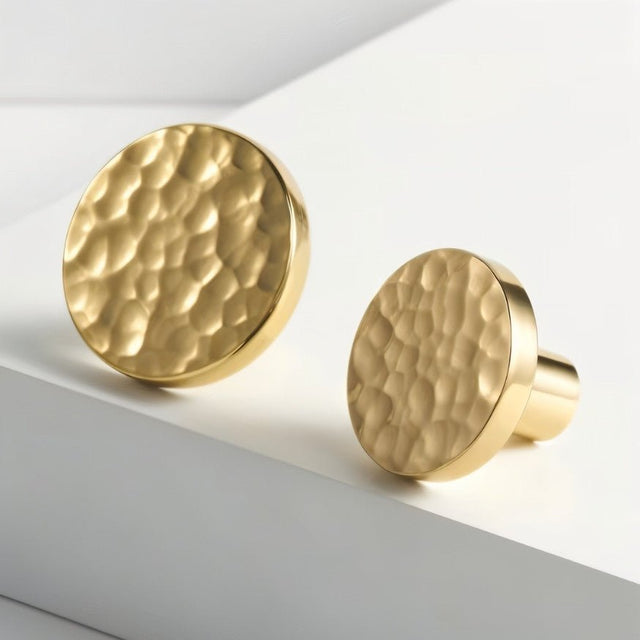 "Pair of hammered brass knobs with a textured, artisanal finish, showcasing their design for cabinetry and drawers."