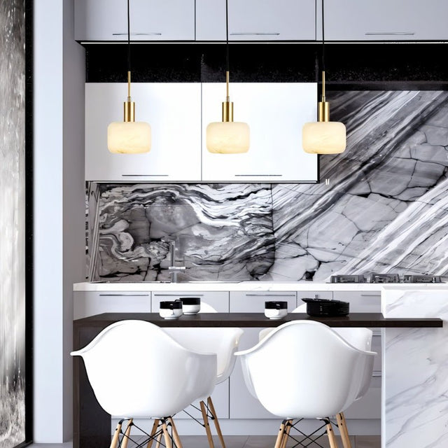 "Three modern pendant lights with rounded alabaster shades and brass accents hanging above a kitchen island with a marble countertop."