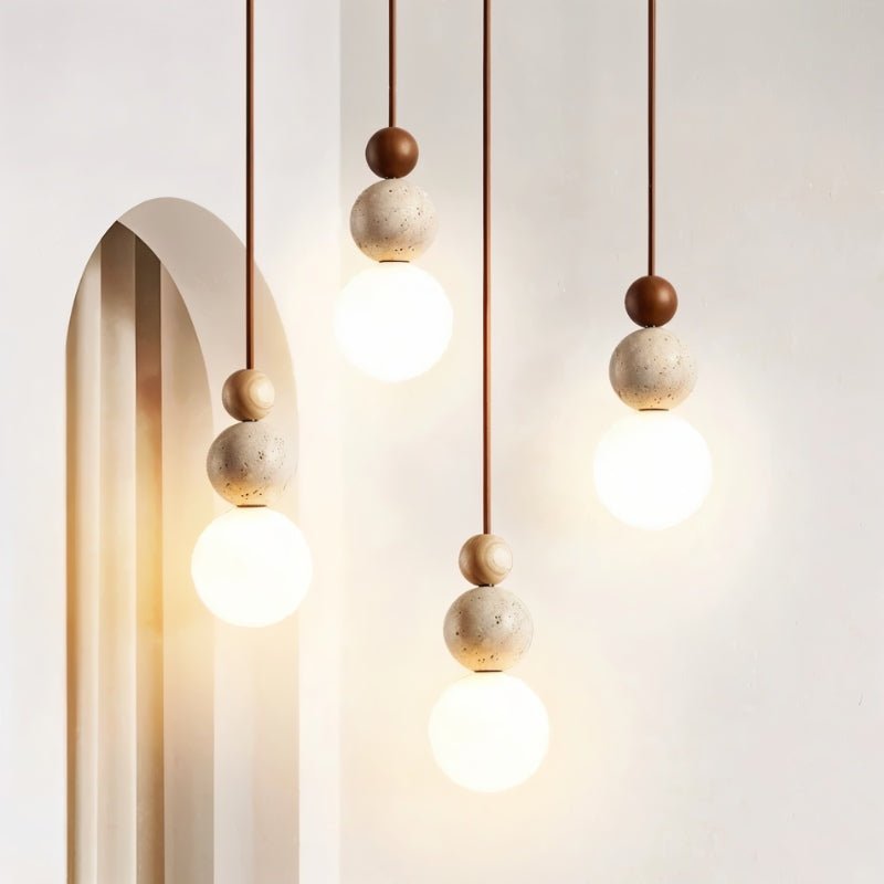 "Group of three sculptural pendant lights with stacked travertine, wood, and metal elements, featuring frosted glass diffusers."