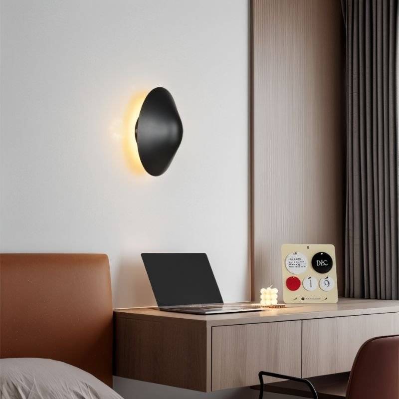 Rochi Wall Lamp in black aluminum installed above a desk, providing ambient lighting in a modern interior setting.