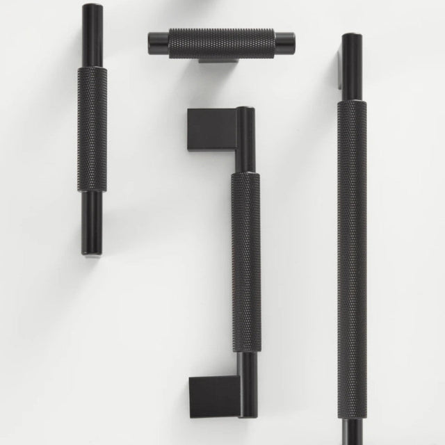 "Set of black knurled brass knobs and pull bars with clean edges, blending industrial design and functionality for modern spaces."