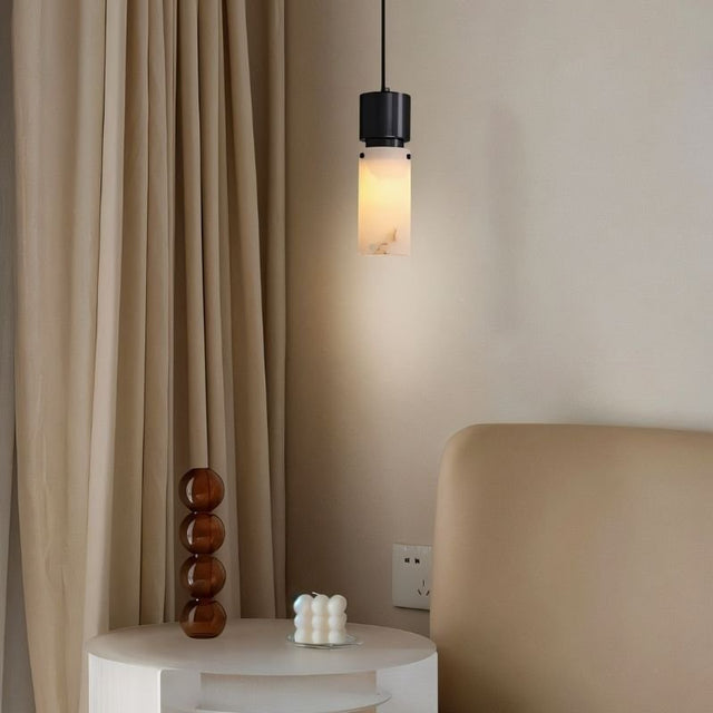 "Modern pendant light with a cylindrical alabaster shade and a black frame, providing a soft glow in a bedroom setting."