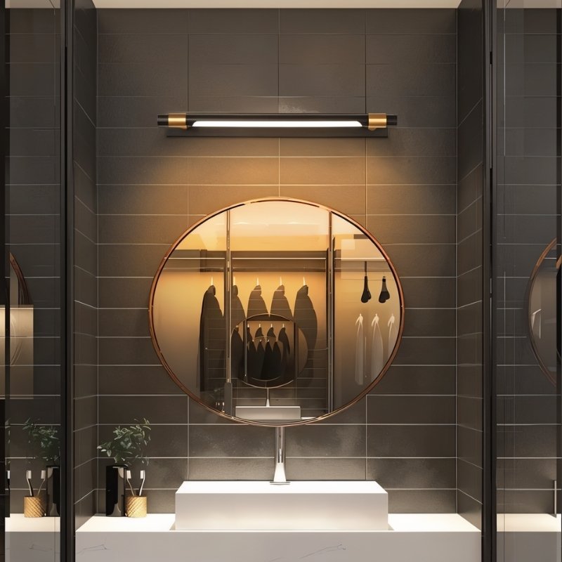"A modern black and gold wall lamp with a cylindrical light bar mounted above a round mirror in a contemporary bathroom."