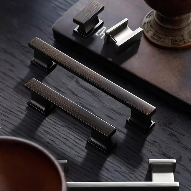 "Set of bronze zinc alloy knobs and pull bars with angular design, displayed on a dark surface."