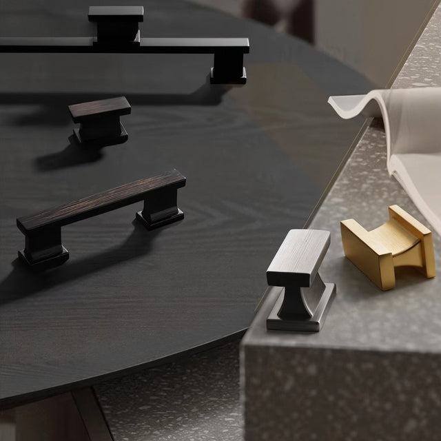 "Set of zinc alloy knobs and pull bars in black, brown, silver, and gold with angular design, displayed on different surfaces."