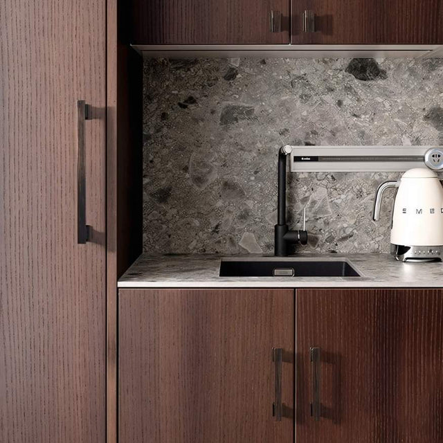"Black zinc alloy pull bars with angular design on dark wood kitchen cabinets with a grey marble backsplash."