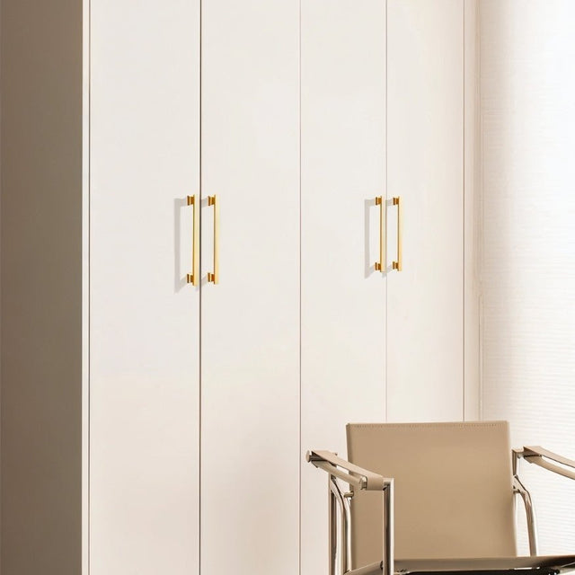 "Gold zinc alloy pull bars with angular design on white wardrobe doors with a chair in the foreground."