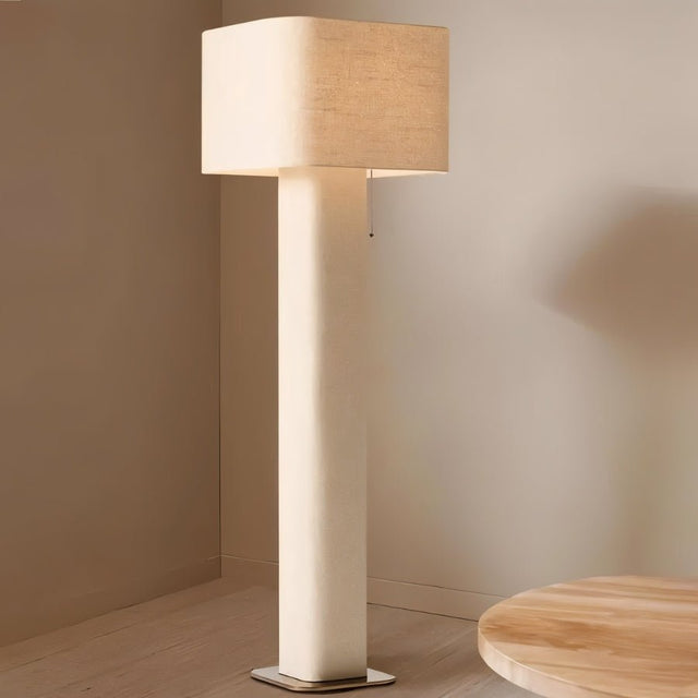 "Modern floor lamp with a cylindrical iron base and a fabric shade in the corner of a living room, next to a round wooden table."