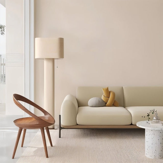 "Modern floor lamp with a cylindrical iron base and a fabric shade in a minimalist living room with a wooden chair and a sofa."