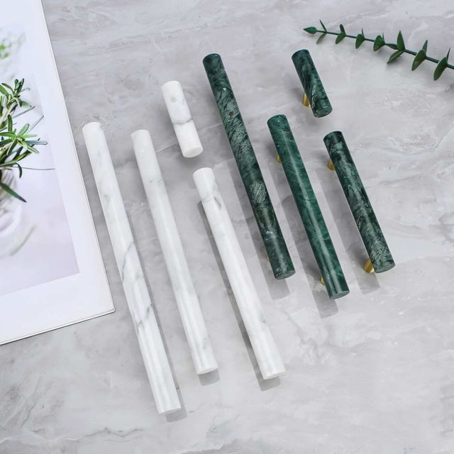 "Assortment of marble and brass knobs and pull bars on a marble countertop, showcasing modern hardware."