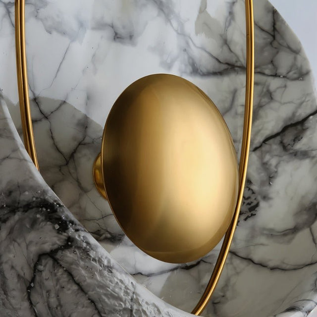 "Close-up of a modern wall lamp with gold sphere, metal hoop, and resin shell with marble veining."