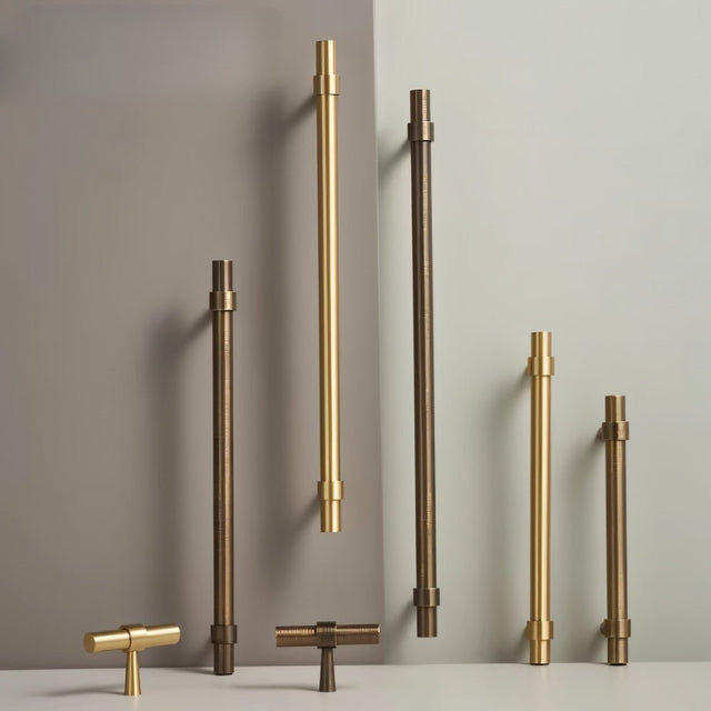 "Set of gold and antique brass pull bars with cylindrical design and subtle accents, arranged on a grey and white surface."