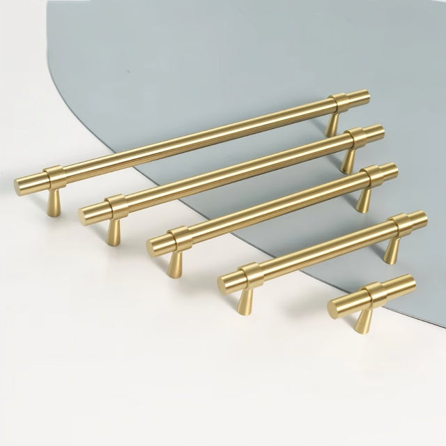 "Set of gold brass pull bars with cylindrical design and subtle accents, arranged on a white and light blue surface."