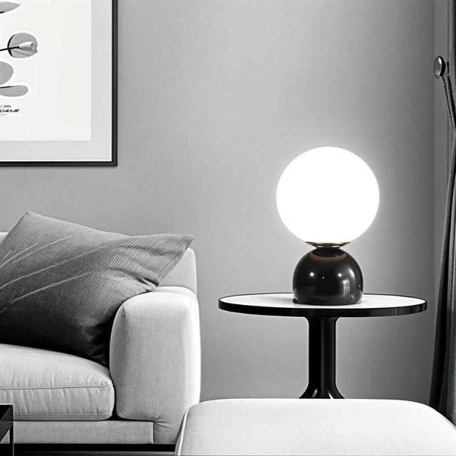 Sibwa Table Lamp on a black side table in a grey-toned living room, offering elegant ambient lighting with a modern touch.