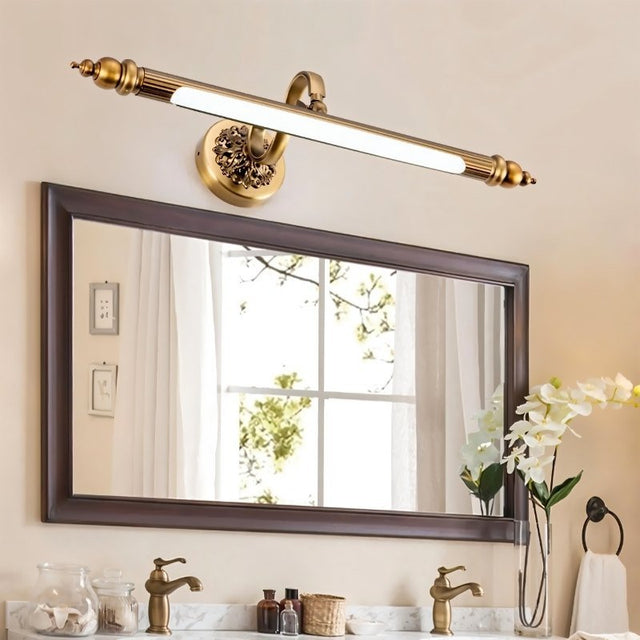 "A retro copper wall lamp with intricate detailing and an elegant rod-shaped light fixture, mounted above a rectangular bathroom mirror with a white countertop and double sinks."