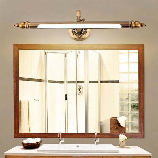 "A retro copper wall lamp with intricate detailing and an elegant rod-shaped light fixture, mounted above a rectangular bathroom mirror with a white countertop and double sinks."