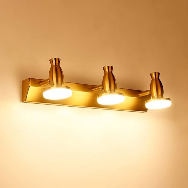 "A modern, 3-head vanity light in a brushed gold finish, illuminated and mounted on a wall."