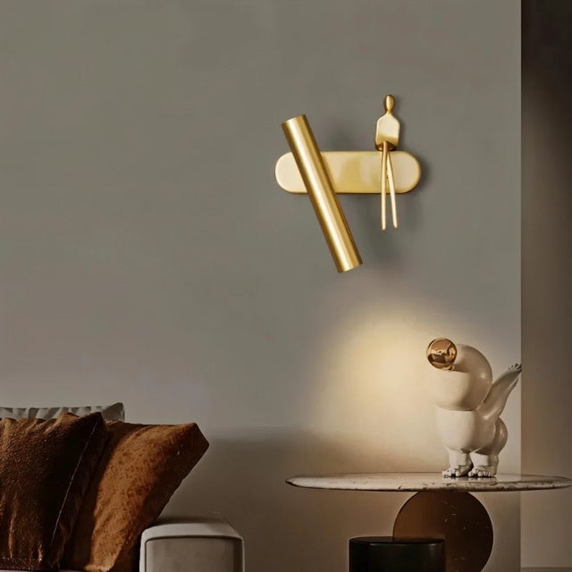 "A gold bedside reading lamp with a figurine on a wall in a living room with a sculpture."