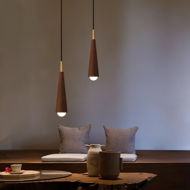 "Pair of modern pendant lights with wooden shades and copper accents hang over a living room seating area."