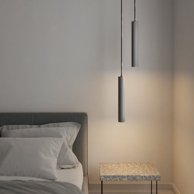 "Two gray cylindrical pendant lights hanging above a bed and a patterned nightstand in a bedroom."