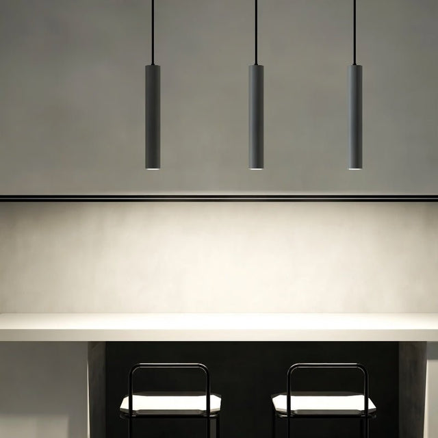 "Three gray cylindrical pendant lights hanging above a kitchen island counter with two black stools."