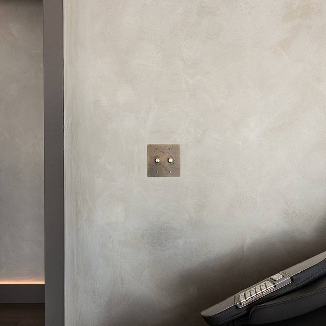 Two-gang The Brass Dimmer Switch - Open Box mounted on a textured wall in a modern interior, near a treadmill.
