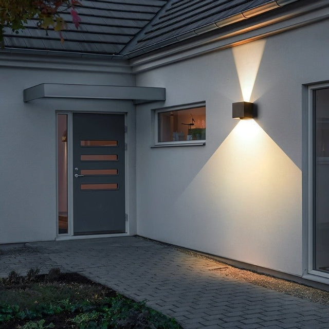 "Tine Wall Lamp installed on an entryway wall, casting upward and downward light beams, made from durable gypsum and aluminum, highlighting the minimalist design."