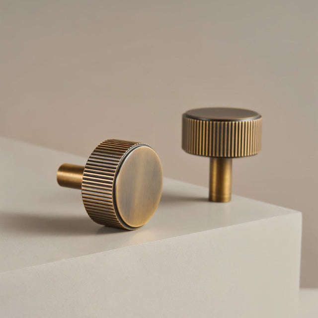 "Pair of modern brass knobs with a sleek ribbed texture, suitable for cabinet doors and drawers in modern and transitional interiors."