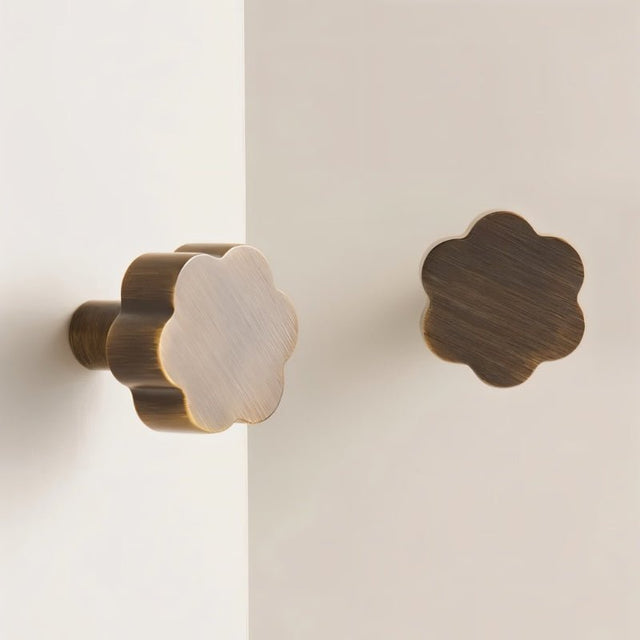 "Two brass floral knobs with brushed finish on a white cabinet."