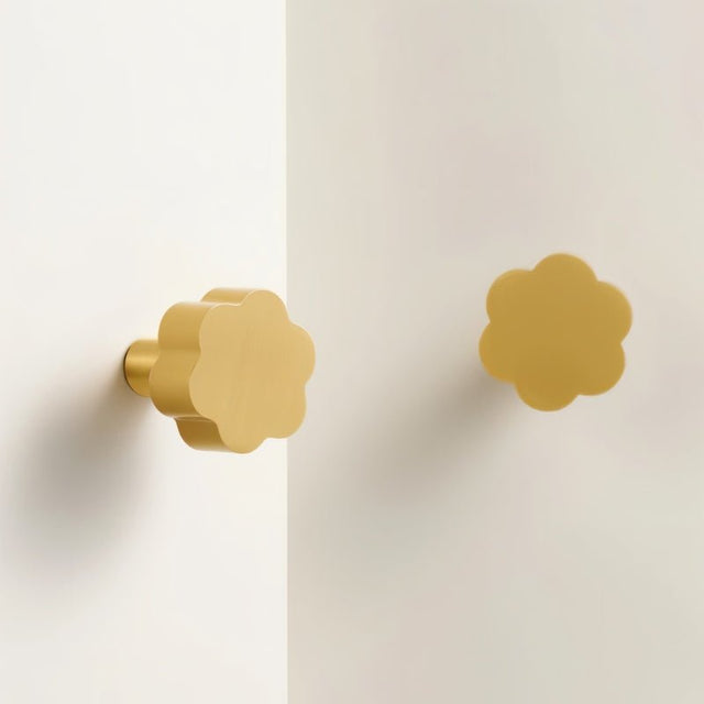 "Two gold brass floral knobs with brushed finish on a white cabinet."