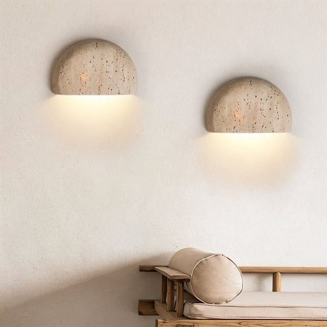 "Pair of minimalist, semi-circular travertine wall lamps flanking a modern sofa, providing soft, ambient lighting."