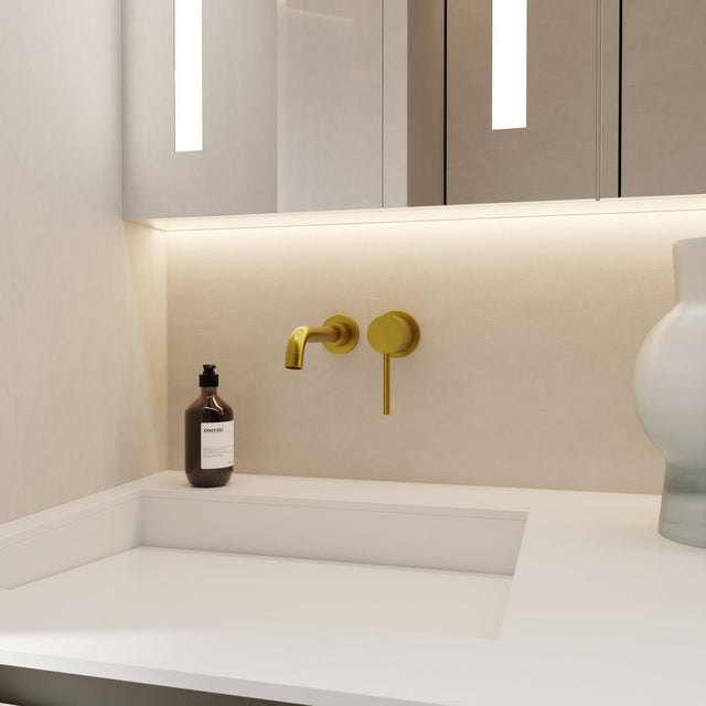 Vartay Bathroom Faucet in brushed gold finish, wall mounted above a modern white sink in a minimalist bathroom setting.