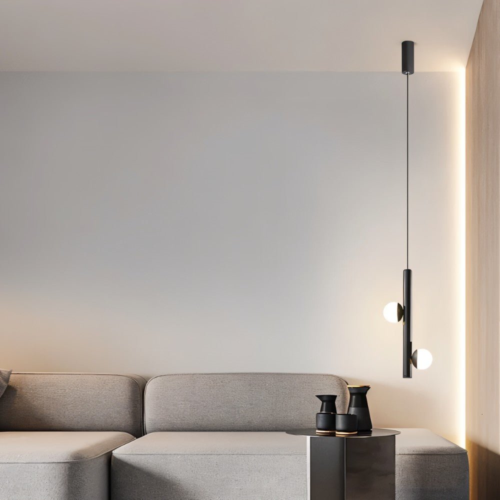 "A minimalist modern living room featuring a sleek iron and acrylic pendant light with cylindrical rods and glowing orb accents, hanging above a gray sofa."