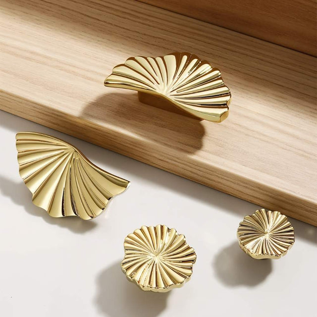 "A group of gold brass fan-shaped drawer pulls in different orientations on a light surface."
