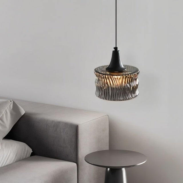 "A pendant light with a rippled glass shade beside a bedroom side table."