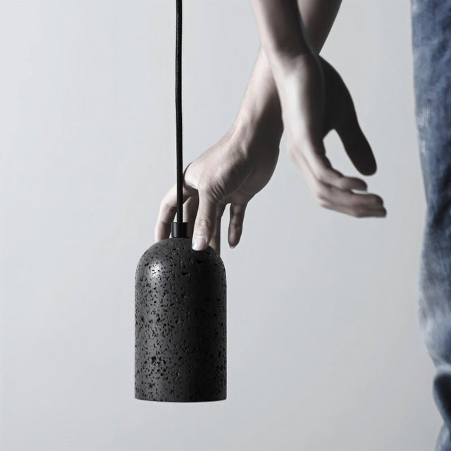 "Person holding a modern cylindrical pendant light crafted from black travertine, showcasing its natural, textured surface and contemporary design."