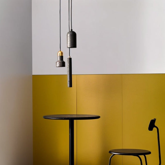 "Modern cylindrical pendant light crafted from black travertine with a textured surface, hanging above a round dining table."