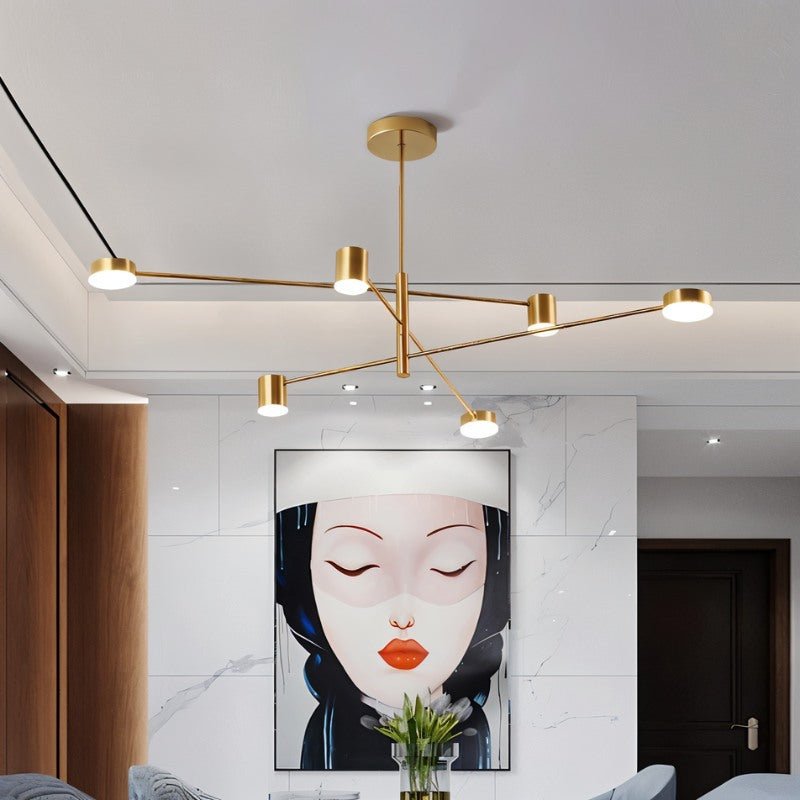 "A gold chandelier with multiple arms extending in different directions, each with a small, round light at the end, shown installed on a white ceiling above a framed painting of a woman's face."