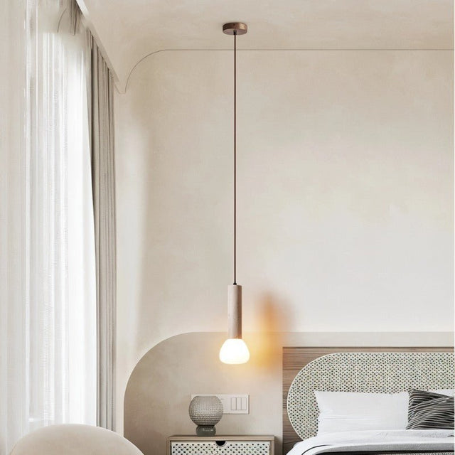"Cylindrical travertine pendant light with a frosted glass diffuser, hanging in a bedroom with a textured wall."