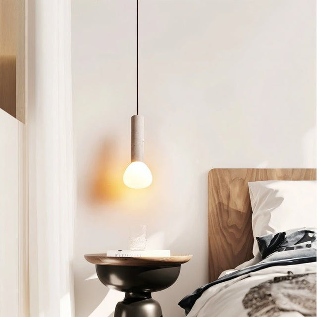 "Single cylindrical travertine pendant light with a frosted glass diffuser, hanging above a bedside table."