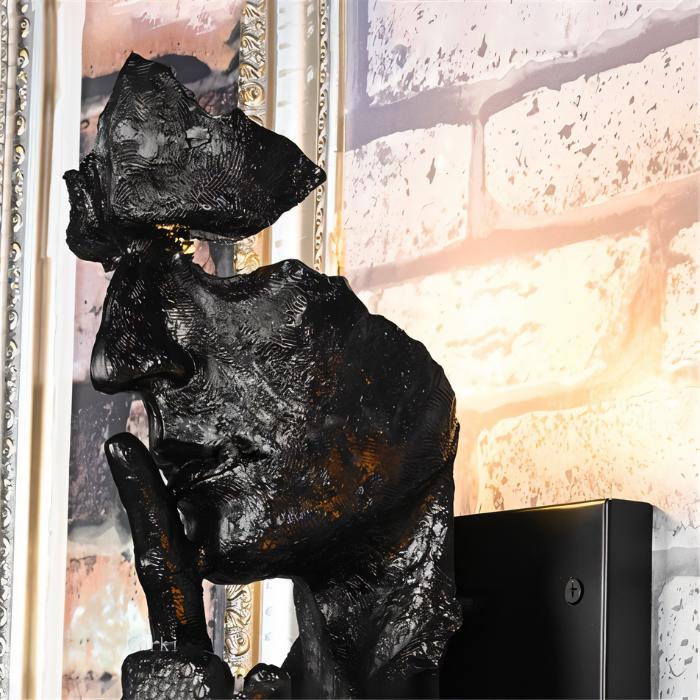Black textured wall lamp mounted beside framed desert landscape artwork on cream-colored wall.