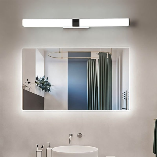 "A silver wall lamp with a linear LED bar illuminating a modern bathroom with a rectangular mirror reflecting a shower curtain and a round sink below."